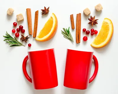 Two red mugs, orange slices, cinnamon sticks, cranberries, and star anise arranged decoratively around them
