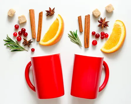 Two red mugs, orange slices, cinnamon sticks, cranberries, and star anise arranged decoratively around them