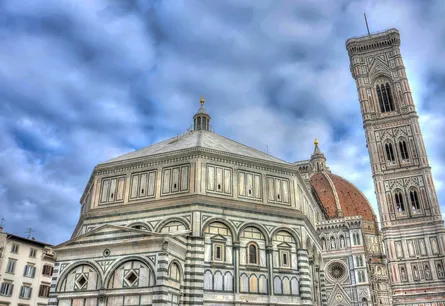 Tall white building with a tower and dome, to the right of it is another large building, both are under a cloudy sky