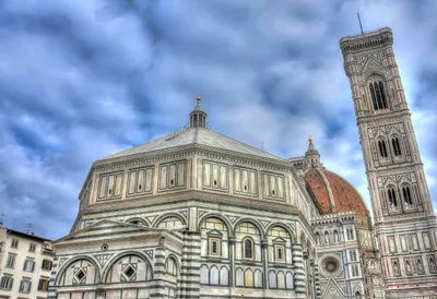 Tall white building with a tower and dome, to the right of it is another large building, both are under a cloudy sky