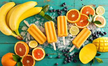 Frozen fruit popsicles with oranges, bananas and blueberries on top of ice