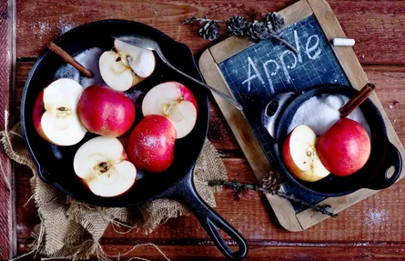 Freshly sliced apples, black cast iron skillet, white chalkboard with 'apple' written on it