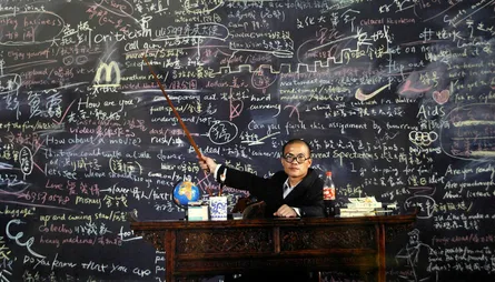 Chalkboard full of writing, man pointing at it