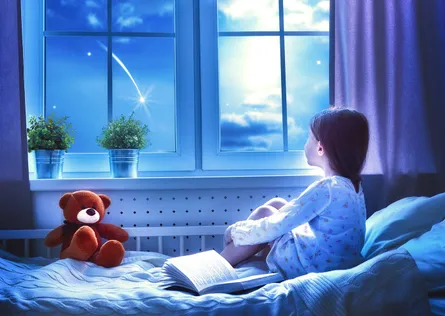 Girl sits on bed looking out window
